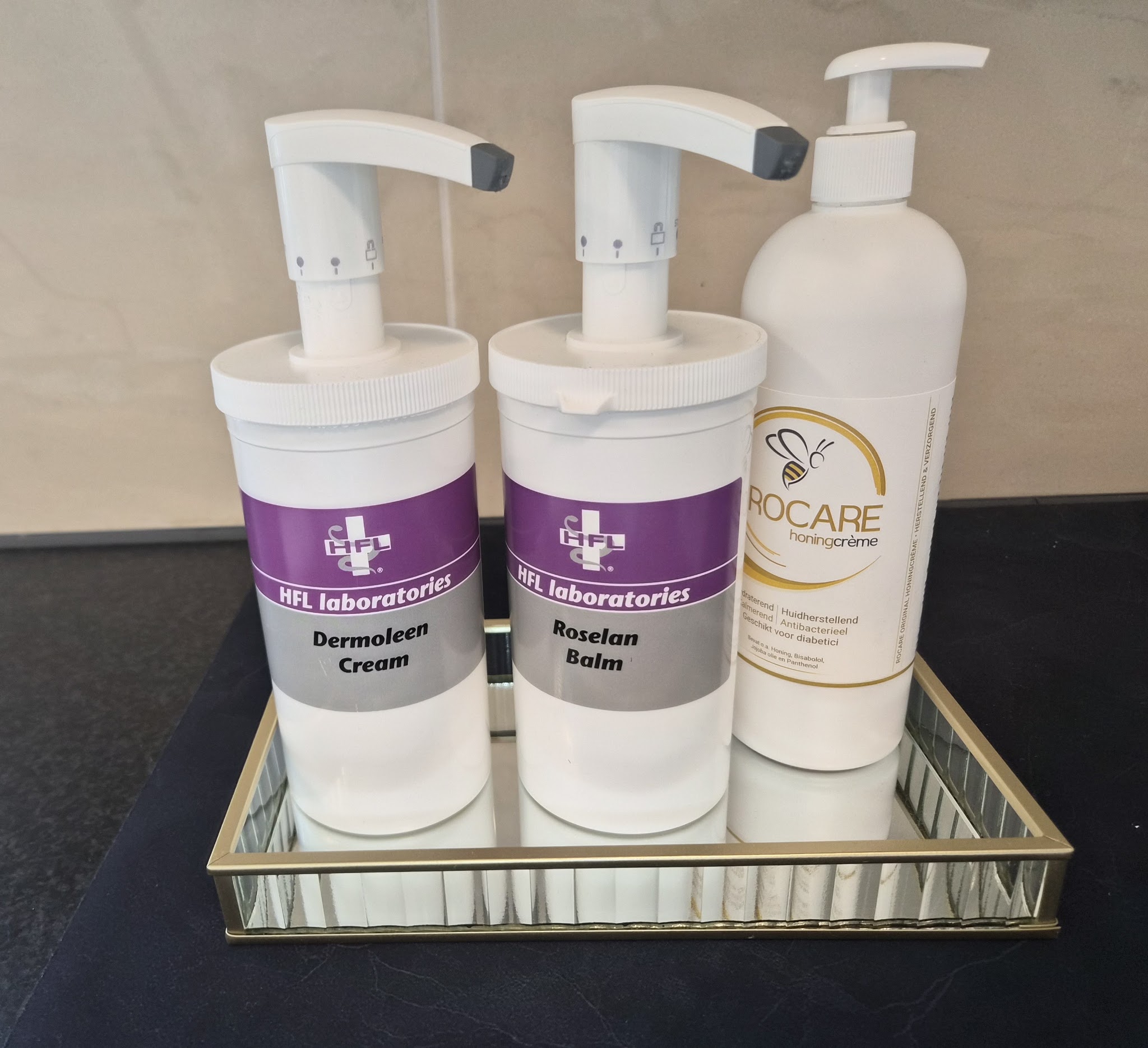 Pompflacons met Dermoleen Cream, Roselan Balm en Biocare op een spiegelblad