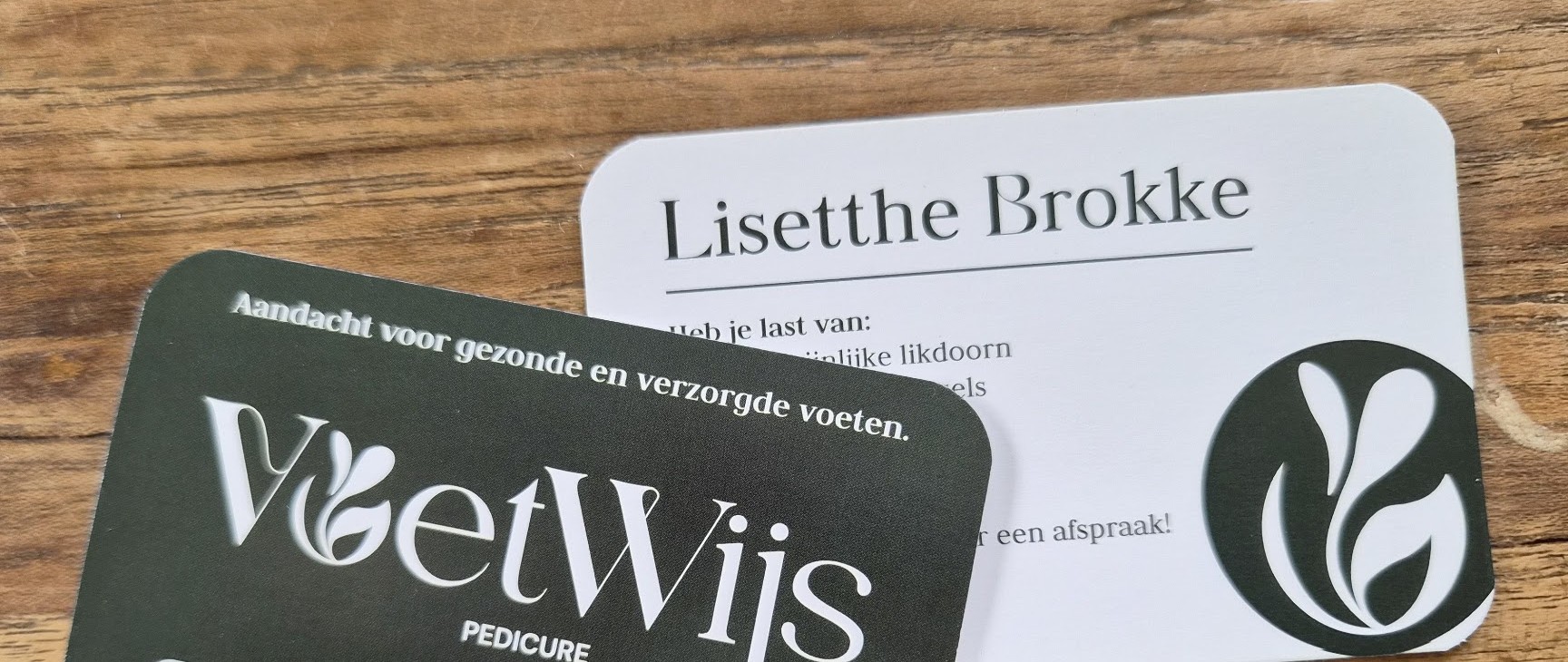 De visitekaartjes van VoetWijs pedicure en Lisetthe Brokke op een houten tafel